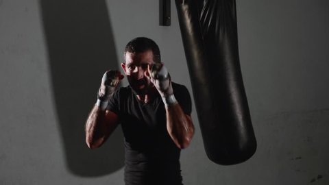 Male bearded boxer exercising shadow boxing. Fighter training punching in the darknes in slow motion.