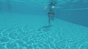 A young guy swims underwater in a swimming pool on a blue background. Underwater video.