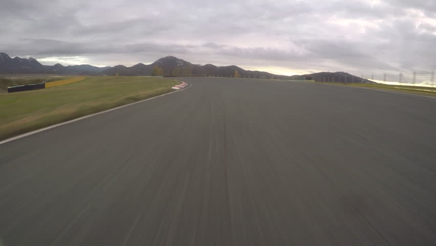 POV: Driving a fast car along the scenic asphalt racetrack on a cloudy evening. Breathtaking first person view of racing a supercar through the long turns of a modern circuit. Adrenaline joyride. Royalty-Free Stock Footage #1016343901