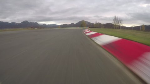 POV: Driving a fast car along the scenic asphalt racetrack on a cloudy evening. Breathtaking first person view of racing a supercar through the long turns of a modern circuit. Adrenaline joyride.
