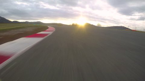 POV: Cinematic view of driving a fast car down an empty raceway at beautiful sunrise. Gentle golden sun rays shine on asphalt racetrack from behind the horizon during an adrenaline filled track day.