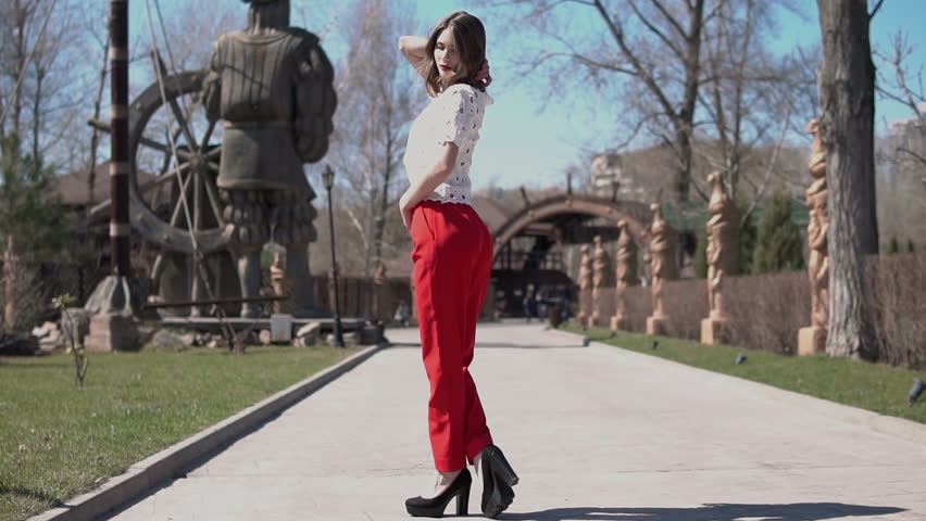 Beautiful model goes through the city on foot. Looking on the outskirts of the city. Charming young woman with a magnificent golden hair, big blue eyes, gorgeous red lipstick and stylish look.