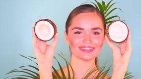 Beauty girl with Coconut. Skincare, cosmetics. Beautiful young woman portrait. Coconut fruit oil and green palm tree leaf on blue background. Healthy Food, skin care concept. Vegan food. Slow motion