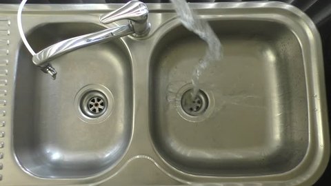 Clean water being tipped into a metal sink in slow motion.