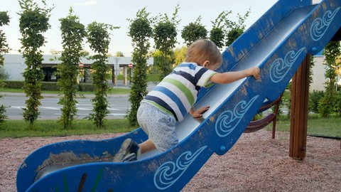4k video of little toddler boy trying to climb on high slide at playground