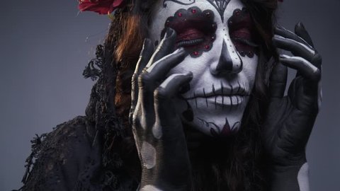 Mystic girl in the makeup of a skull with flowers and cobweb pulls her hands towards the camera