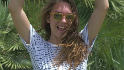 Portrait of funny girl. Woman going crazy. Raising her hands and shout. Showing peace sign. Posing on exotic green background. In casual clothes and sunglasses. 4k