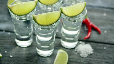 From above tequila shots served with lime and salt on wooden table with pepper 