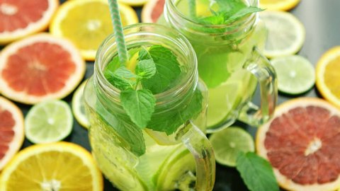 From above shot of few glass jars filled with lime lemonade and mint leaves composed on table among slices of citrus fruit