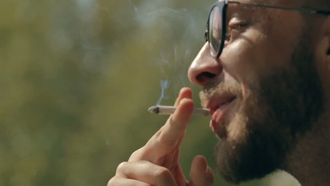 Man smoking a rolled up cigarette. Close up shot of man's hand and mouth. Man smoking a joint with tobacco.