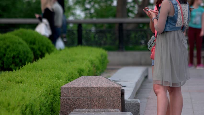 Two girls with smartphones in the park. Modern lifestyle od young people. Female legs, outdoors.
