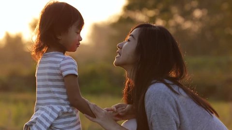 mother and her daughter kidding and enjoying sunset with hands up in a meadow