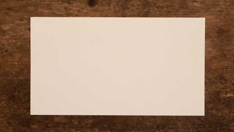 Unwrapping and wrapping a piece of paper on wooden background. Folding and unfolding of blank paper note on wood panel. Stop motion animation. Seamless loops.