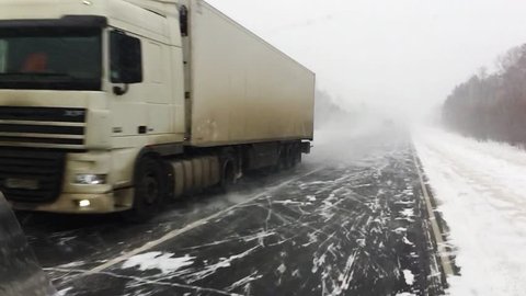 The car is on a snow-covered highway.
Heavy truck with trailer carries cargo. 
Winter road with a gusty wind and a snowstorm, slow motion. 