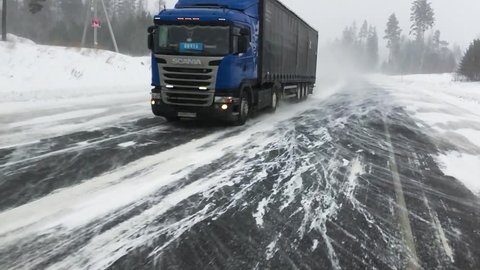 The car is on a snow-covered highway.
Heavy truck with trailer carries cargo. 
Winter road with a gusty wind and a snowstorm, slow motion. 