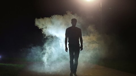 The man walking near the cloud of smoke on the dark background, slow motion