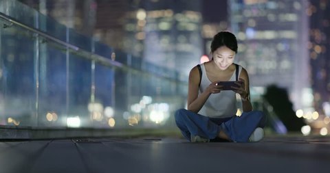 Woman play game on cellphone and sitting on ground at night