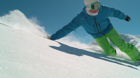 SLOW MOTION CLOSE UP: Smiling boarder snowboarding in mountains on sunny winter day. Freeride snowboarder riding powder snow past the camera, doing hand drag on fresh snow surface. Backcountry skiing