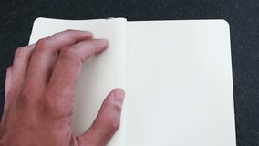 A man's hand writes in a white notebook 