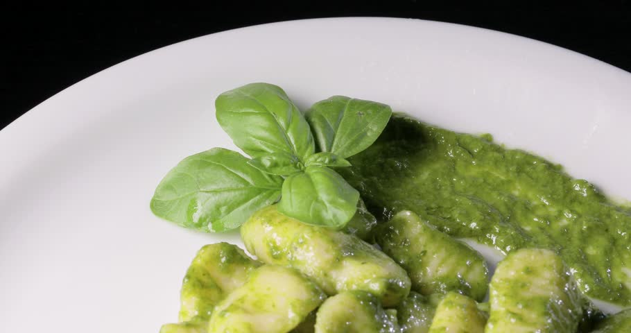 Vegetarian green potato gnocchi with fresh basil pesto arranged on a rotating plate.
