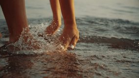 Woman scooping smooth salty water into her hands and dropping it, waterdrops splashing, hitting glossy sea surface. Young girl playing in ocean at dreamy golden sunset