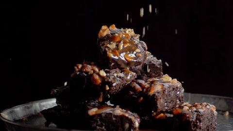 Pouring nuts onto brownie in slow motion. Arm takes peace of brownie