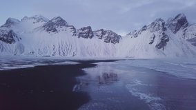 Drone video from a winter and snowy scene at the famous Stokksnes also known as Vestrahorn in Iceland. Photographers at the beach photograph the mountains.