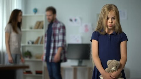 Sad little girl looking her parents arguing on background, problems in family