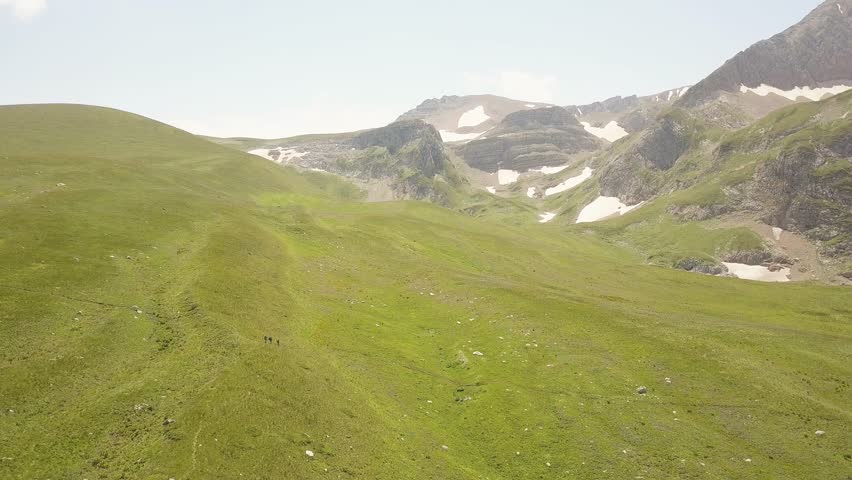 People walking on summer meadow in valley and mountain landscape from drone