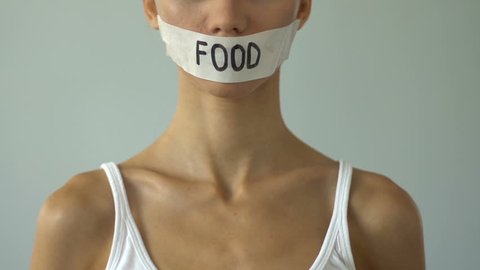 Girl with taped mouth holding empty plate, food restriction causes anorexia