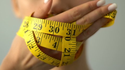 Closeup of girl closing mouth with measuring tape, bmi calculation, anorexia