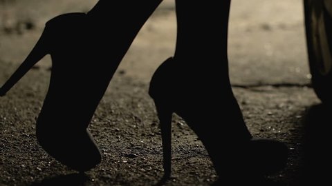 Seductive woman on high heels slowly walking to car night street, escort service