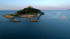 Drone flies around St Michaels Mount Cornwall behind during beautiful golden hour revealing full moon. 