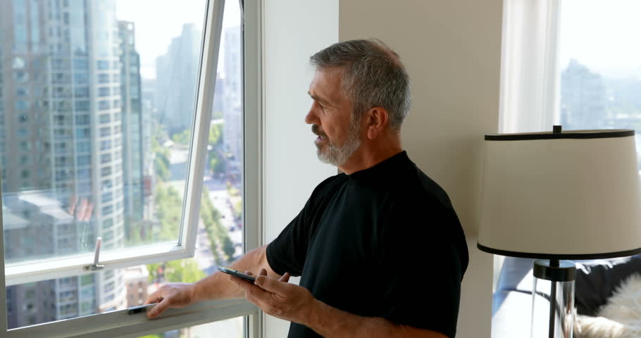 Man taking on mobile phone while standing near window at home 4k. Social distancing and self isolation in quarantine lockdown for Coronavirus Covid19