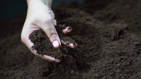 Farmer hand holding and pouring black organic soil in slow motion