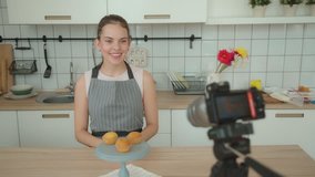 Modern woman shoots a video of the process of making dessert - a capcake confectionery vlog. Culinary blog: young woman decorates a capcake with a cream, using a pastry bag, and comments her actions.