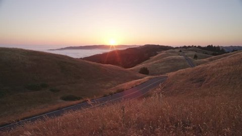 A car drives down an isolated road along the coast of the beautiful California countryside at sunset