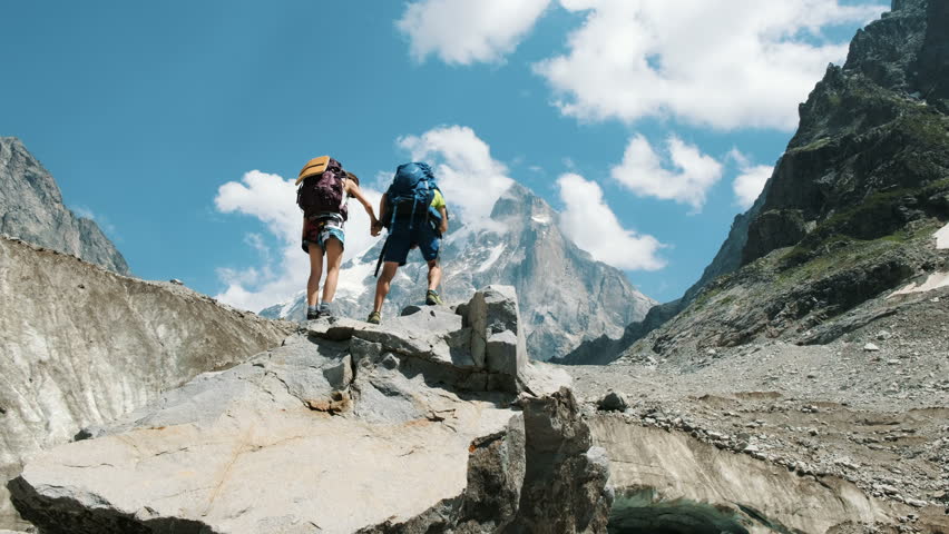 Couple of tourists with backpacks in the campaign raise their hands up on the top of the mountains. Concept of victory, achievement of the goal and success