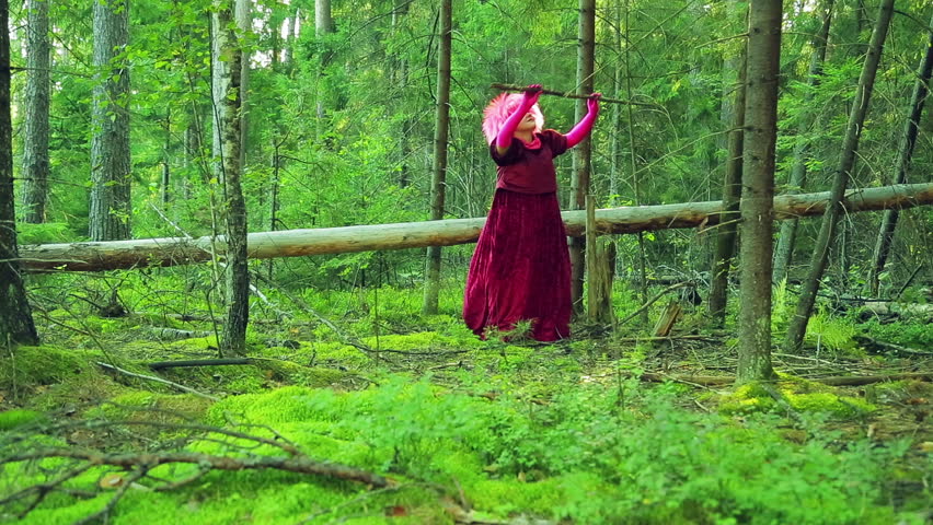 A young witch in red in the forest will twist his staff over his head.