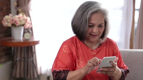 Cheerful senior asian woman using her smart phone at home