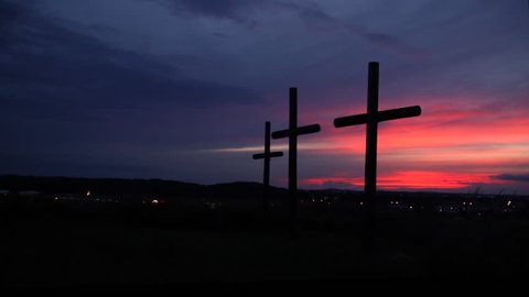 A silhouette of three crosses overlooking a city view during a beautiful pink sunset.