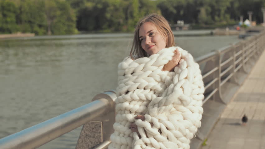 The girl is walking around the city lake, wrapped in a white plaid of merino wool in the early autumn.