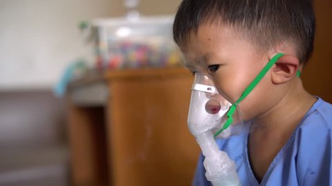 Sick Asian boy about 2 years and 8 months in hospital uniform using inhaler containing medicine to stop coughing from disease like flu or RSV, Respiratory Syncytial Virus