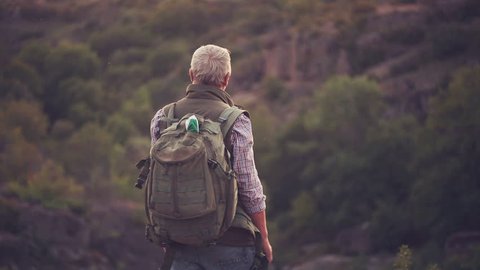 Senior bearded man with a backpack looking at a mountains and nature
