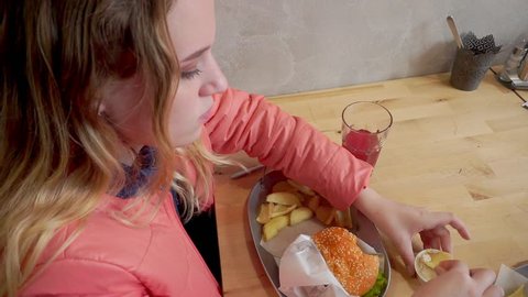 A young girl eating a hamburger. Sitting at a table in a cafe. View from the top