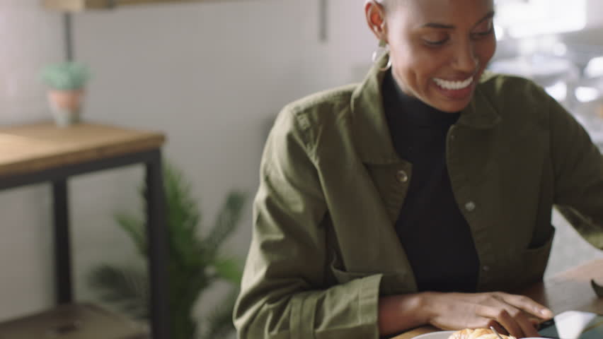 happy african american woman using tablet computer showing friend laughing together enjoying funny entertainment on mobile device screen in coffee shop