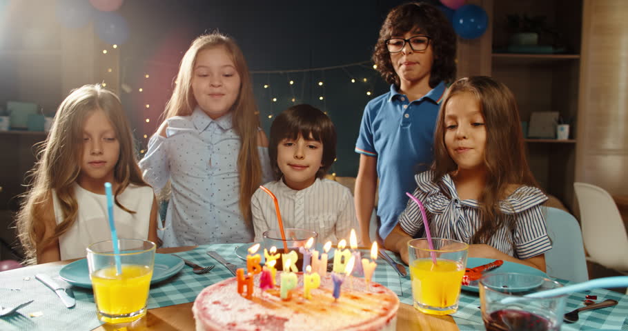 Children having birthday party, blowing out the candles on birthday cake. Group of kids celebraing birthday of their friend, cheering, having fun - happy childhood concept 4k