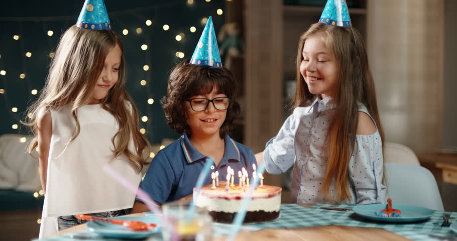 Kids at birthday party. Three little friends excited to blow out the candles on bithday cake, and cheering, having fun - happy childhood concept 4k