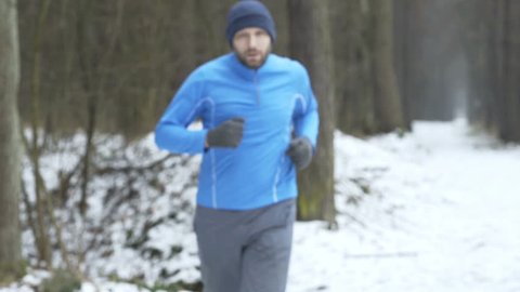 Young man jogging in winter forest and checking time on phone
