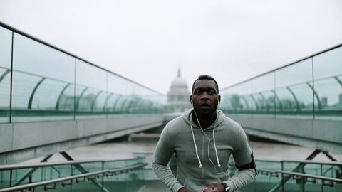Young sporty black man runner with smart phone running on the bridge in London.